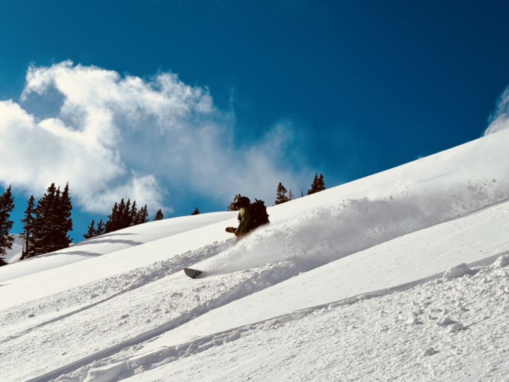 Snowboarder carving through deep powder on a sunlit Colorado slope